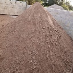 Wilk-trans Maciej Wilk - Kupa brązowego piasku w skrzyni samochodu ciężarowego, widoczne drobne grudki i zróżnicowana tekstura.