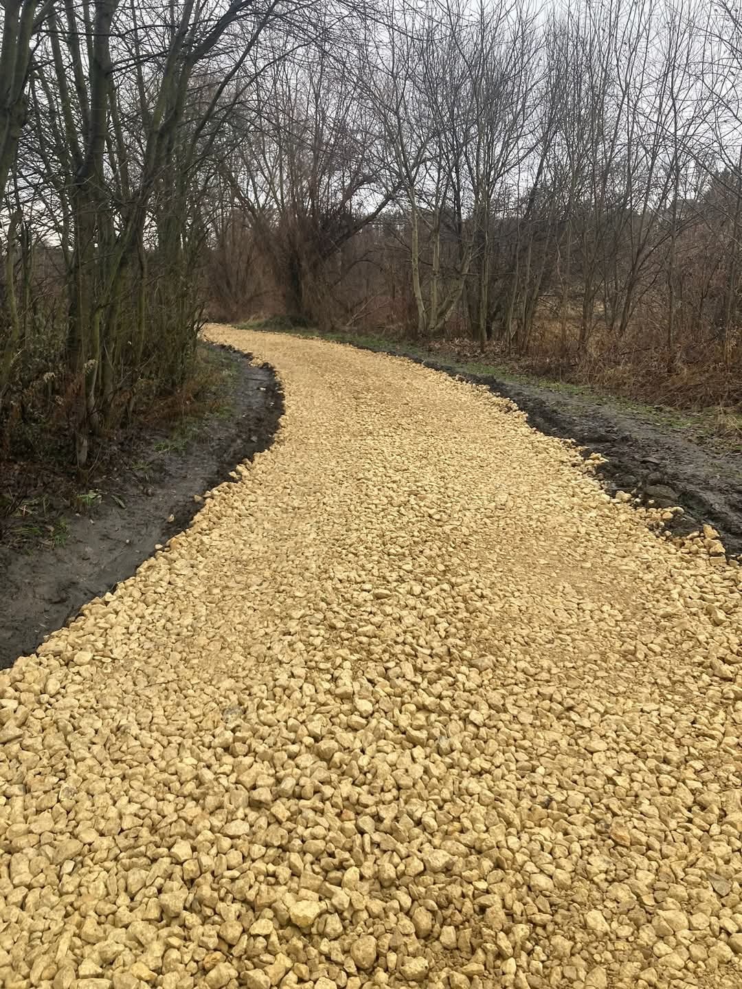 Nowo utwardzona, kręta ścieżka z jasnych kamieni w naturalnym otoczeniu leśnym, widoczne błotniste obrzeża.