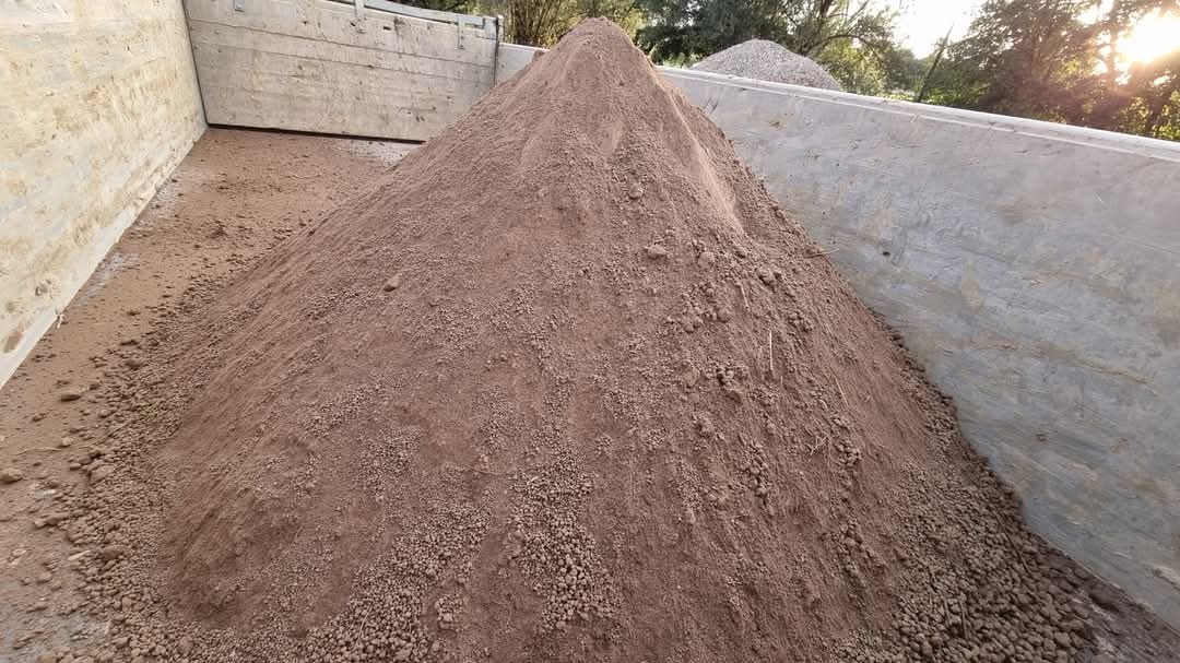 Kupa brązowego piasku w skrzyni samochodu ciężarowego, widoczne drobne grudki i zróżnicowana tekstura.