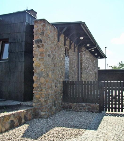 Elewacja budynku usługowego w Łomży z fragmentami wykończonymi kamieniem rzecznym i drewnianą okładziną, widoczna drewniana brama wjazdowa.