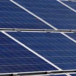 Rząd paneli słonecznych z wyraźną strukturą krzemową i srebrnymi ramami, ułożonych pod kątem na dachu, widoczne mocowania.