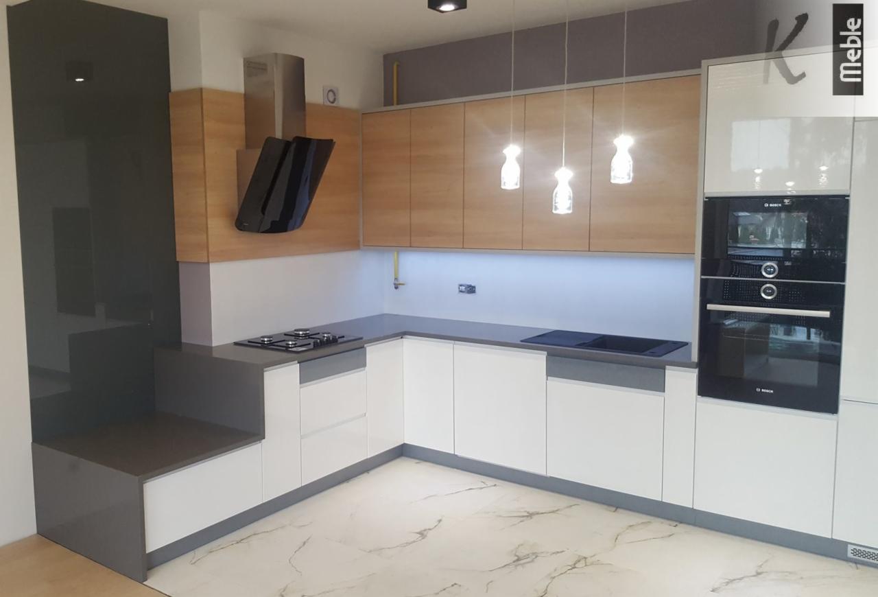 Nowoczesna kuchnia w kształcie litery L z białymi frontami szafek dolnych i drewnopodobnymi górnymi, szary blat, płyta gazowa i indukcyjna, piekarnik i mikrofalówka w zabudowie, marmurowa podłoga...