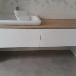 Nowoczesna łazienka z umywalką nablatową na drewnianym blacie i białymi szafkami pod spodem, wzorzyste płytki na ścianie.