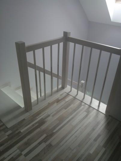 Biała balustrada z pionowymi szczebelkami przy schodach z białymi stopniami i podłogą w odcieniach szarości, widok z góry.