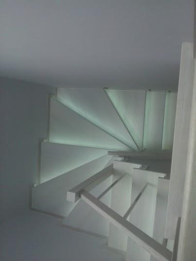 Spiralne, białe schody z podświetleniem LED wzdłuż stopni, widok z dołu, minimalistyczny design.