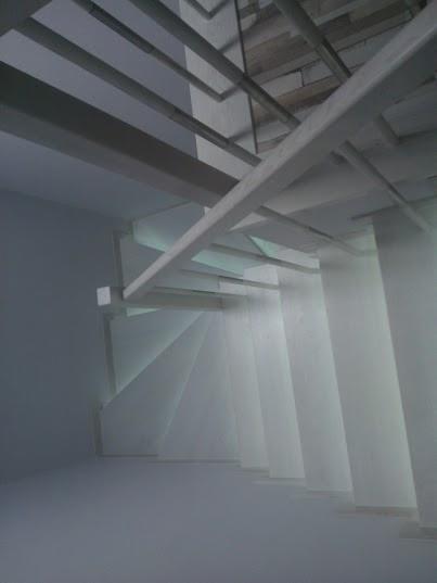 Minimalistyczne, spiralne schody z białego betonu, widziane z dołu, z widoczną konstrukcją nośną sufitu.