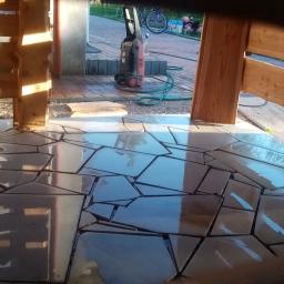 Jar-bud - Ułożony taras z nieregularnych, ciemnych płyt kamiennych, częściowo mokry po czyszczeniu, widoczny fragment drewnianej konstrukcji z surowego drewna i myjka ciśnieniowa w tle.