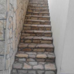 Jar-bud - Zewnętrzne schody z nieregularnego kamienia prowadzące w górę, przylegające do ściany z kamienia i ściany budynku pokrytej tynkiem.