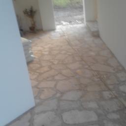 Jar-bud - Wnętrze w trakcie wykańczania, z podłogą wyłożoną nieregularnymi płytami kamiennymi i widocznymi workami z zaprawą przy ścianie.