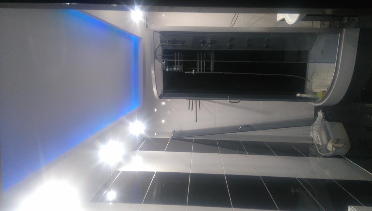 Ukończona łazienka z czarno-białymi płytkami, kabiną prysznicową z hydromasażem i podświetlanym sufitem w kolorze niebieskim.