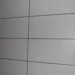 Szare, prostokątne płytki ścienne z ciemnymi fugami, sąsiadujące z brązową boazerią imitującą drewno.