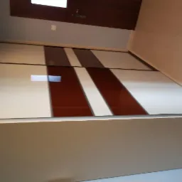 Nowoczesna szafa przesuwna z białymi i brązowymi panelami, widoczna od dołu, z oświetleniem sufitowym odbijającym się na powierzchni.