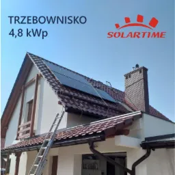 Dom jednorodzinny z zamontowanymi panelami słonecznymi na dachu z dachówki ceramicznej, widoczna drabina oparta o ścianę, logo firmy SolarTime w prawym górnym rogu.