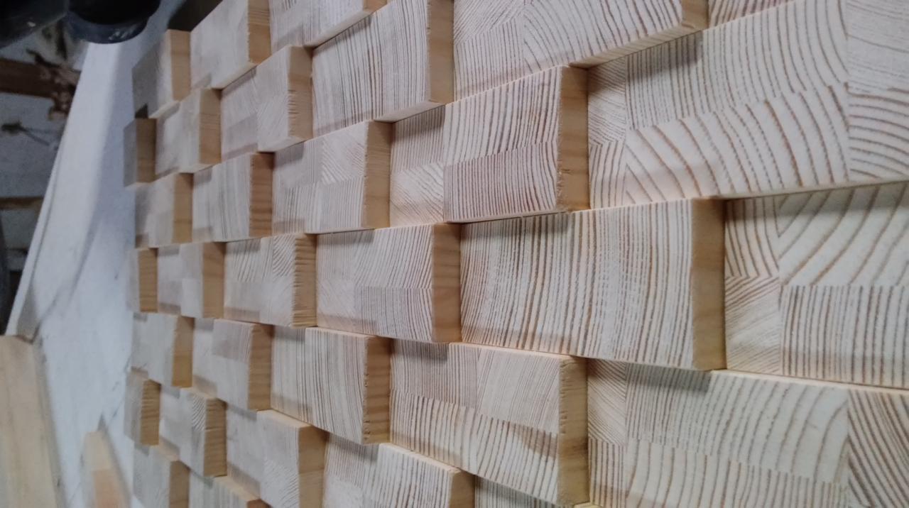 Drewniana mozaika ścienna z jasnych, kwadratowych klocków o wyraźnym usłojeniu, tworzących trójwymiarowy wzór.