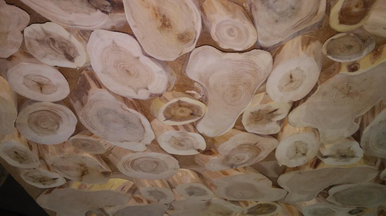 Drewniany sufit dekoracyjny z nieregularnych, jasnych plastrów drewna, ukazujących słoje, wypełnionych piaskową fugą.