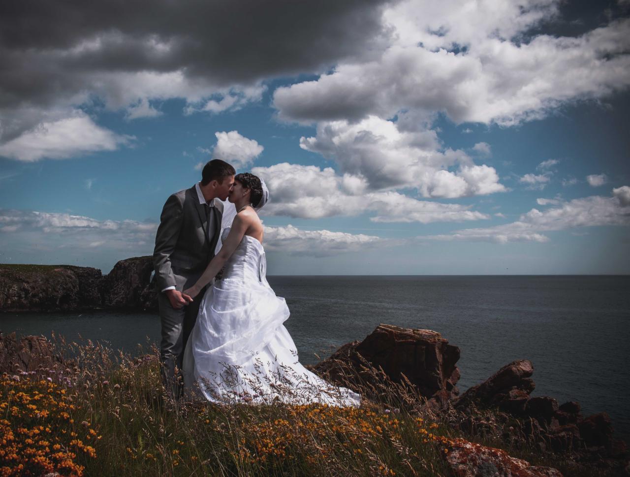 Para młoda całuje się na klifie z widokiem na morze, dramatyczne chmury na niebie.