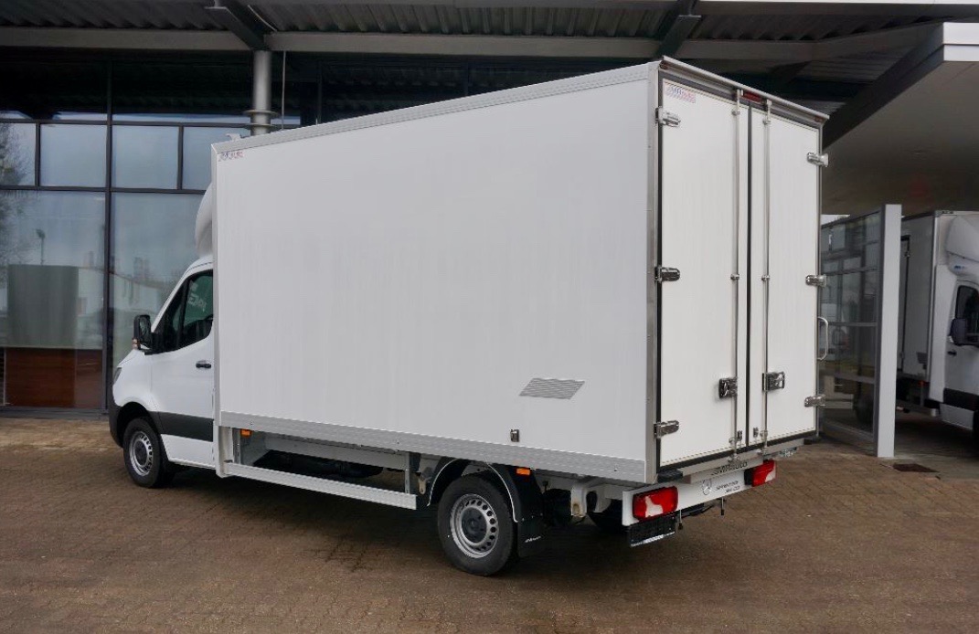 Biały samochód dostawczy z zabudową kontenerową, widok z boku i tyłu, zaparkowany na zewnątrz budynku.