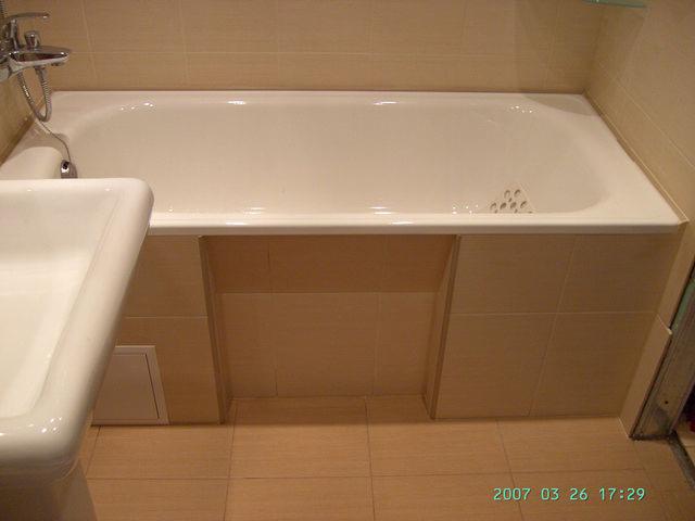 Wanna obudowana beżowymi płytkami ceramicznymi, widoczna umywalka po lewej stronie, całość w jasnej tonacji.