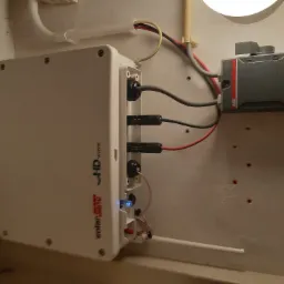 Zamontowany inwerter solarny SolarEdge HD Wave z przewodami i zabezpieczeniami ABB na ścianie z widocznymi śladami po wierceniu.