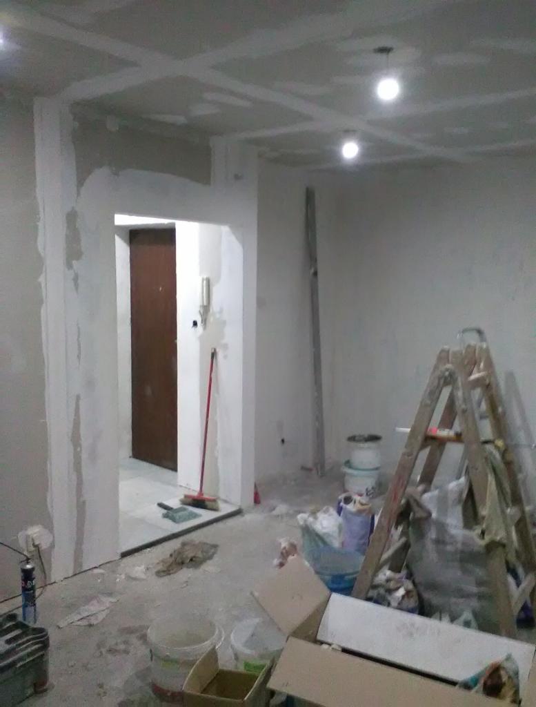 Wnętrze w trakcie remontu: ściany i sufit po szpachlowaniu, widoczne kartony, drabina malarska, wiadro z farbą i narzędzia malarskie.
