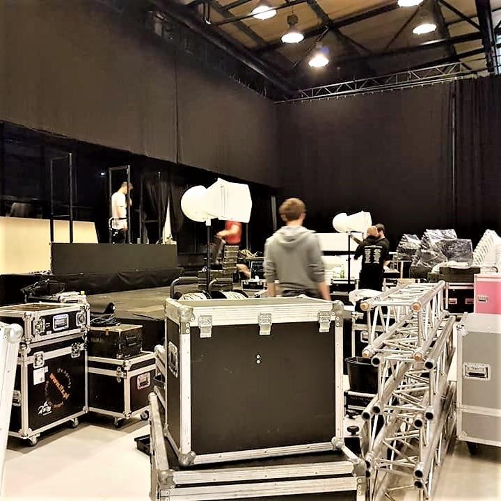 Przygotowania do eventu: montaż sceny, oświetlenia i nagłośnienia przez ekipę techniczną w dużej hali.