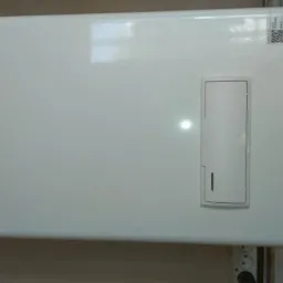 Biały, wiszący piec gazowy Beretta z podłączonymi miedzianymi rurami instalacji grzewczej na tle białych, kwadratowych płytek.