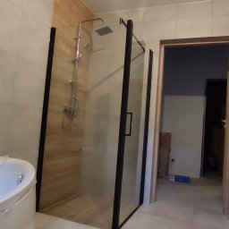 Krzysztof Konig - Nowoczesna łazienka z kabiną prysznicową typu walk-in z czarnymi ramami, owalną wanną i umywalką z szafką w trakcie wykańczania.