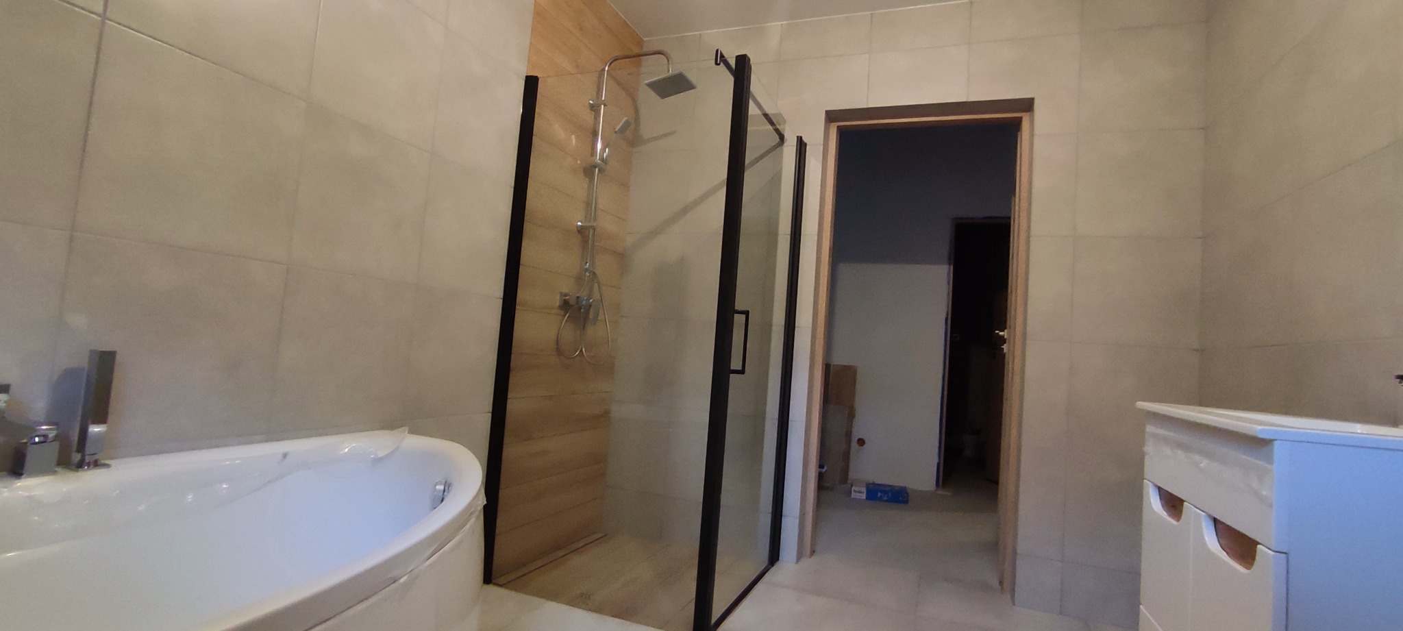 Nowoczesna łazienka z kabiną prysznicową typu walk-in z czarnymi ramami, owalną wanną i umywalką z szafką w trakcie wykańczania.