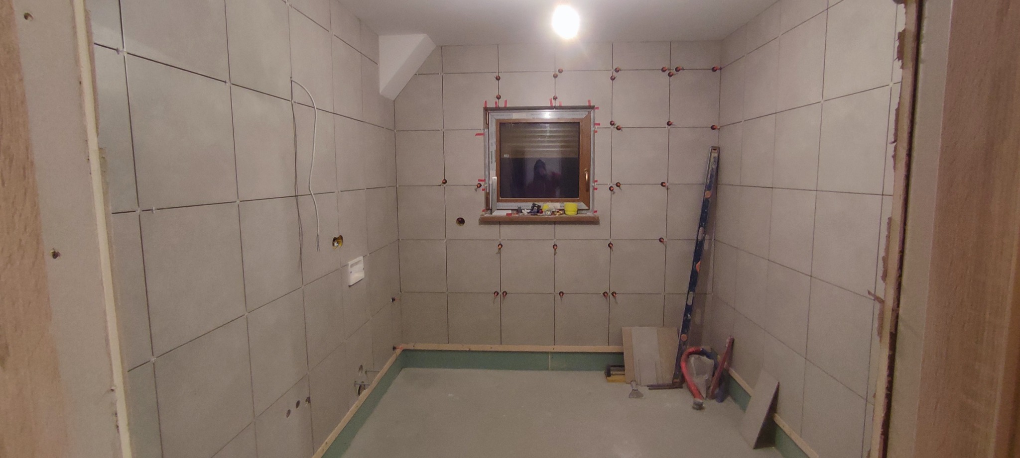 Łazienka w trakcie układania płytek ściennych, widoczne krzyżyki dystansowe, poziomica i narzędzia do glazury