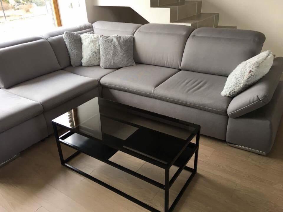 Szary narożnik z poduszkami i czarnym stolikiem kawowym na drewnianej podłodze, schody w tle.