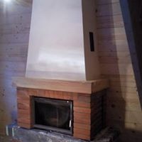 Nowoczesny kominek z ceglaną obudową i jasnym, gładkim okapem, umieszczony na betonowej podstawie w pomieszczeniu wykończonym boazerią.