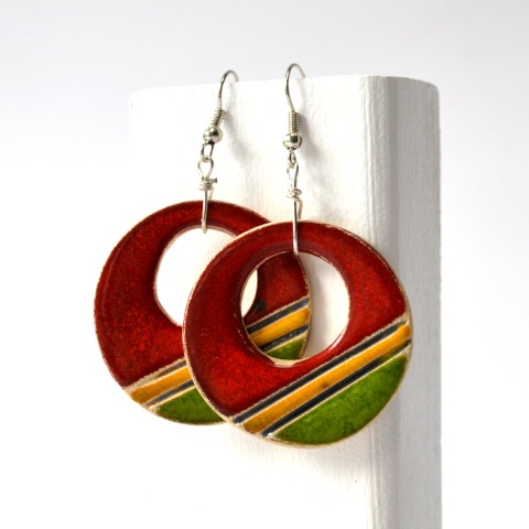 Para wiszących, okrągłych kolczyków z emaliowaną powierzchnią w kolorach czerwonym, zielonym i żółtym, z srebrnymi haczykami, na białym tle.