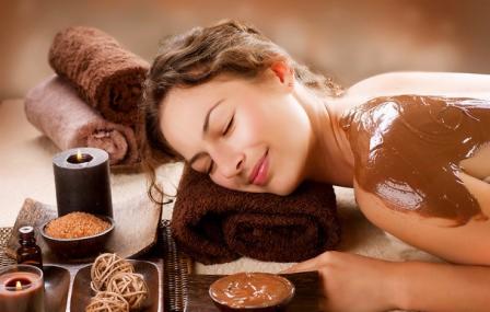 Kobieta z zamkniętymi oczami relaksuje się podczas czekoladowego zabiegu na ciało, leżąc na ręczniku w otoczeniu świec i aromatycznych olejków.