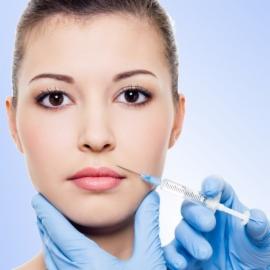 Kobieta podczas zabiegu powiększania ust, igła w pobliżu górnej wargi, ręce w niebieskich rękawiczkach, delikatne oświetlenie, gładka skóra