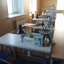 Rząd białych maszyn do szycia marki Typical z czarnymi lampkami, ustawionych w jasnym pomieszczeniu z boazerią i oświetlonych oknami.