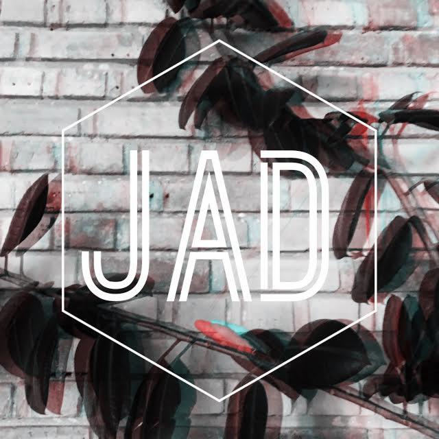 Grafika z napisem JAD w białym heksagonie na tle ceglanej ściany i roślin z ciemnymi liśćmi, z efektem glitch.