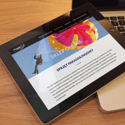 Studio Websteady - Tablet wyświetlający stronę internetową sklepu online ze sprzętem do parasailingu, leżący na laptopie na drewnianym stole.