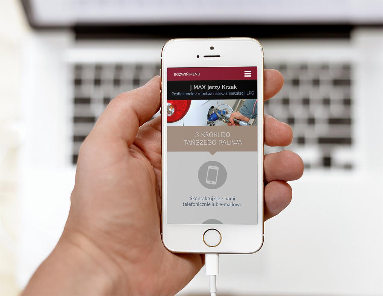 Smartfon w dłoni wyświetlający stronę internetową firmy J MAX Jerzy Krzak oferującej montaż i serwis instalacji LPG, z widocznym menu, zdjęciem instalacji LPG i wezwaniem do kontaktu.
