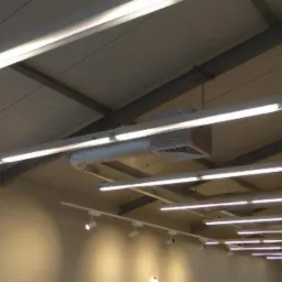 Wnętrze hali z widocznym systemem oświetlenia liniowego LED, elementami wentylacji pod sufitem i stalową konstrukcją dachu w jasnej kolorystyce.