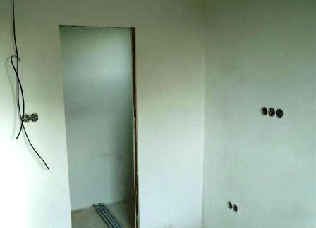 Ściana w trakcie przygotowania do malowania, widoczne puszki elektryczne i przewody, surowa powierzchnia przed ostatecznym wykończeniem.