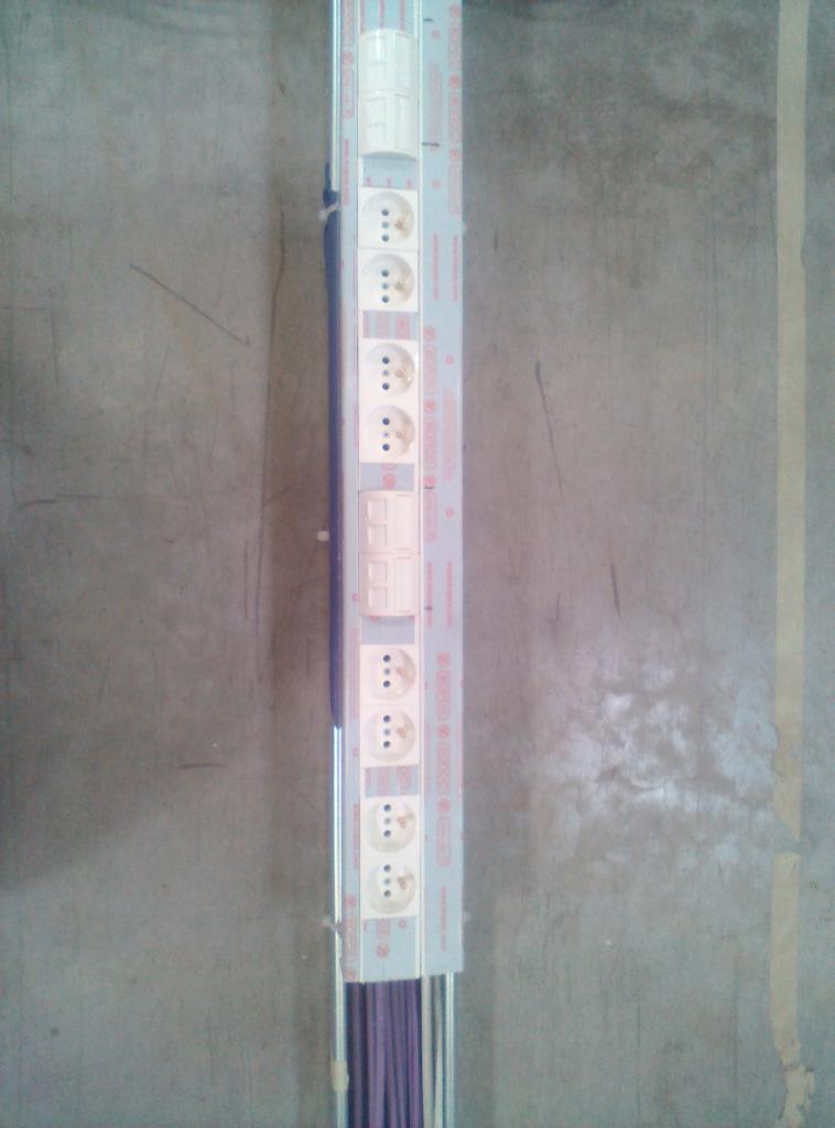 Listwa zasilająca z gniazdkami i włącznikami zamontowana na szarej ścianie, widoczne przewody w dolnej części listwy.