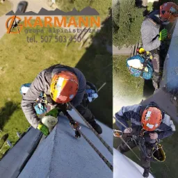 Alpinista przemysłowy w pomarańczowym kasku, zabezpieczony linami, wykonuje prace na elewacji budynku. Widok z góry, z widocznym logo firmy KARMANN.