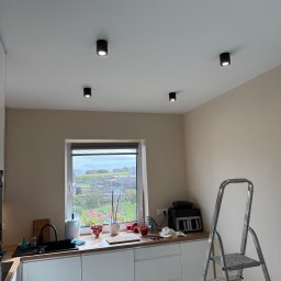 ElektroLuk Łukasz Powała - Kuchnia z czterema punktowymi lampami sufitowymi; drabina oparta o ścianę, okno z widokiem na ogród. Minimalistyczny design.