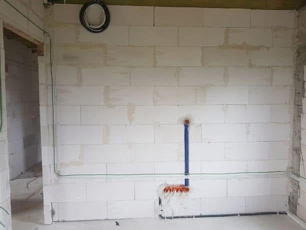 Ściana z betonu komórkowego w trakcie prac instalacyjnych: przewody elektryczne w peszlach i puszki. Widoczne pionowe i poziome trasy kablowe.