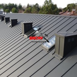 Łącz-dach Paweł Łączyński - Szary dach z blachy na domu jednorodzinnym, widoczne okna dachowe i kominy wentylacyjne. Nowoczesne pokrycie dachowe z wyraźnymi liniami łączeń blachy.