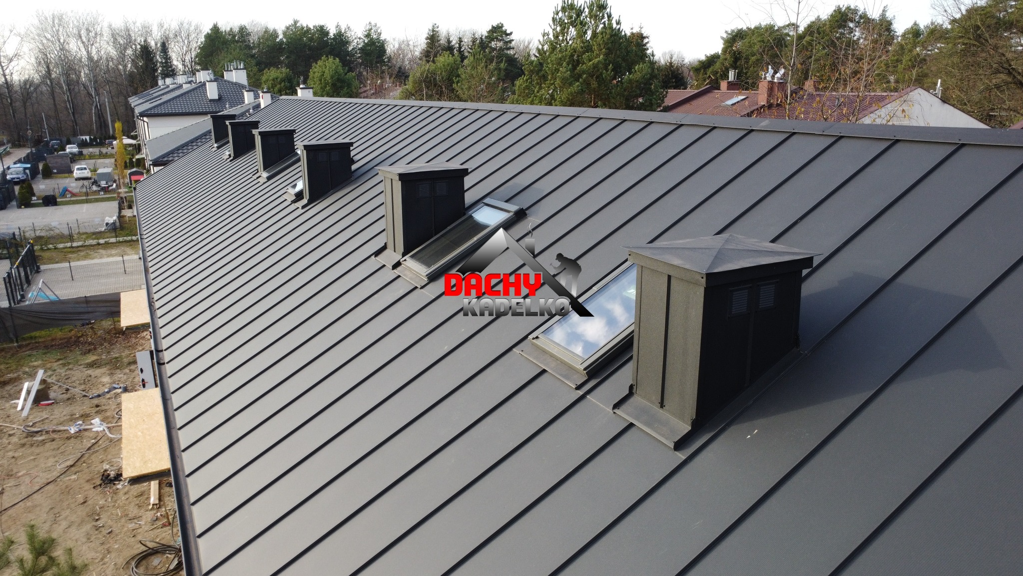 Szary dach z blachy na domu jednorodzinnym, widoczne okna dachowe i kominy wentylacyjne. Nowoczesne pokrycie dachowe z wyraźnymi liniami łączeń blachy.