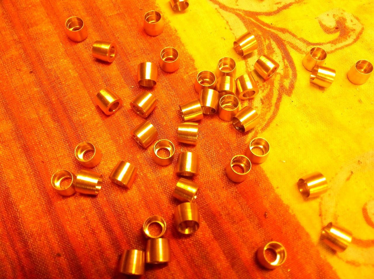 Partia precyzyjnie obrobionych, złotych tulejek z metalu, rozłożonych na pomarańczowo-żółtym tle z delikatnym wzorem.