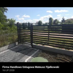 Nowoczesne, poziome ogrodzenie panelowe w kolorze antracytowym, z bramą wjazdową, świeżo zamontowane na posesji z kostką brukową i przygotowanym podłożem pod trawnik.