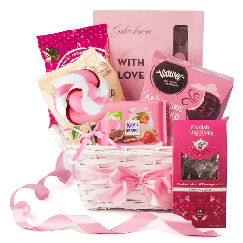 Różowy kosz upominkowy z łakociami: lizak, czekolady Ritter Sport i Wawel, herbata English Tea Shop. Całość przewiązana wstążką, idealna na prezent.