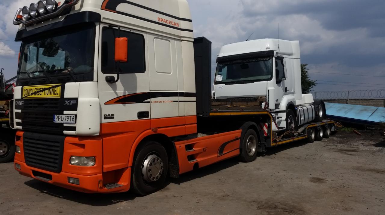 Ciężarówka DAF XF z pomarańczowym dołem transportuje na lawecie ciągnik siodłowy na tle pochmurnego nieba.